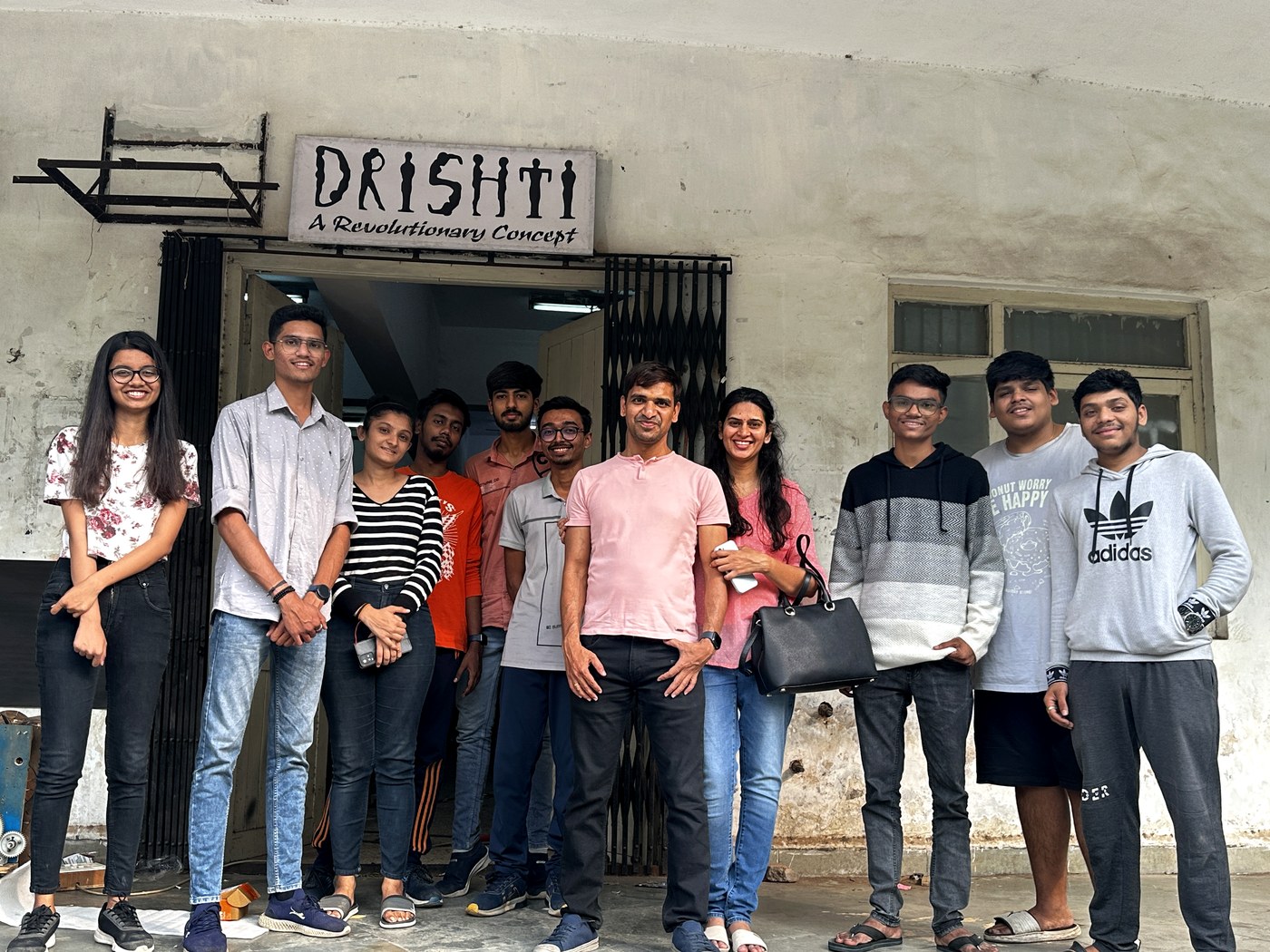 Back at the Drishti door at NIT Surat with the current student team — founded 2002, still run by students, 20+ years on.